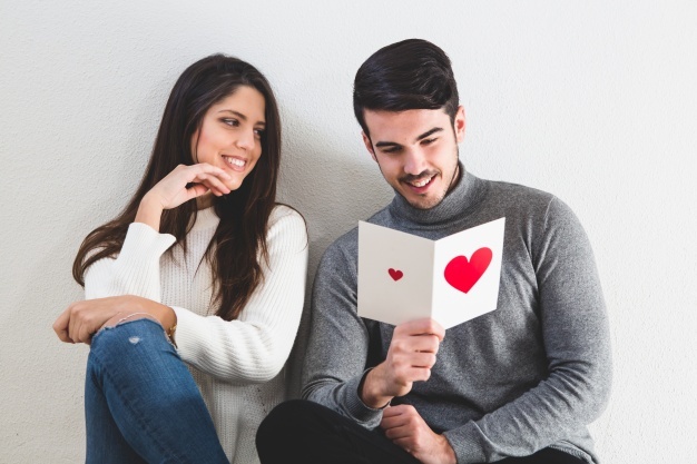 girl smiling while her boyfriend reads a romantic postcard_23 2147596088