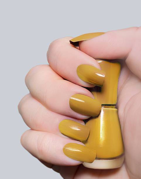 Close up mature woman’s hand with spicy mustard yellow colored nails and nail polish bottle